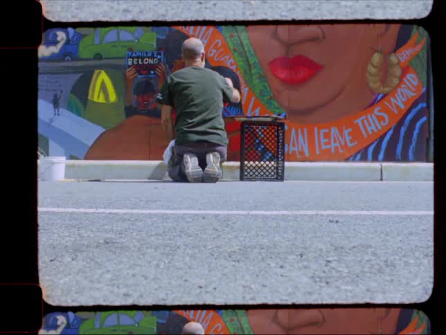 Man crouching down graffitiing a wall next to the street