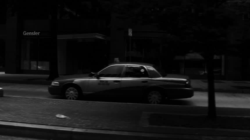 Black and white footage of a taxi driving down a dark street