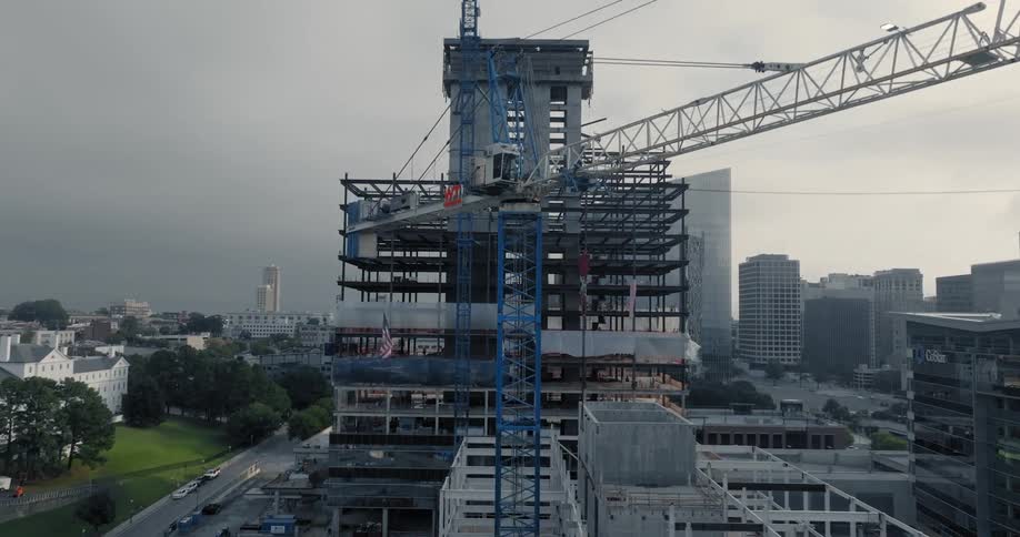 Large construction site with an unfinished highrise building featuring exposed steel beams and a crane next to it