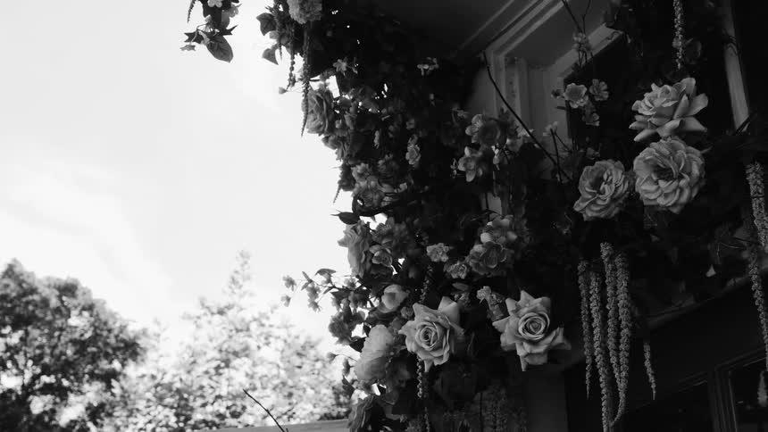 A black and white footage of a doorway or window decorated with a profusion of flowers