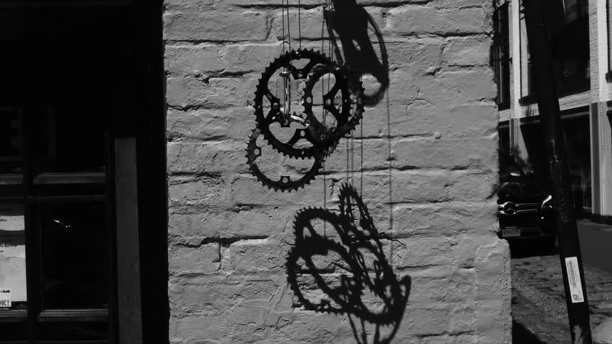 Black and white footage of a brick wall with several bicycle gears hanging from it