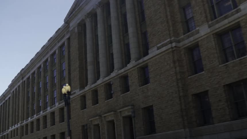 A large imposing building with a row of columns and many windows made of darkcolored brick and illuminated by a lamppost in the foreground