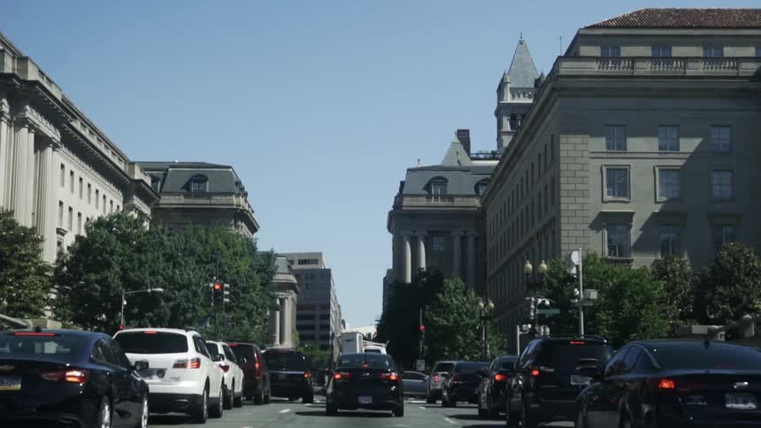 Three lanes of cars stop at a red light at an intersection of a city