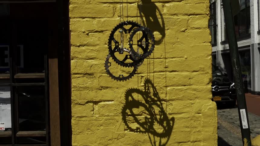 Gears dangling from strings outside a building with a car driving past
