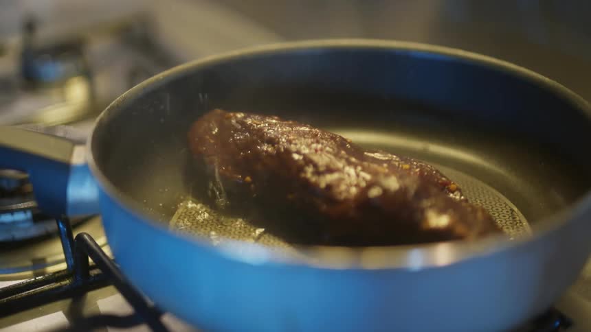 A piece of meat sizzling in a blue pan on a stovetop