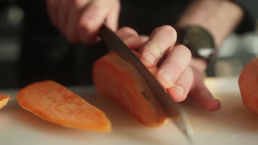 Close up of a mans hands holding a knife and cutting a fruit