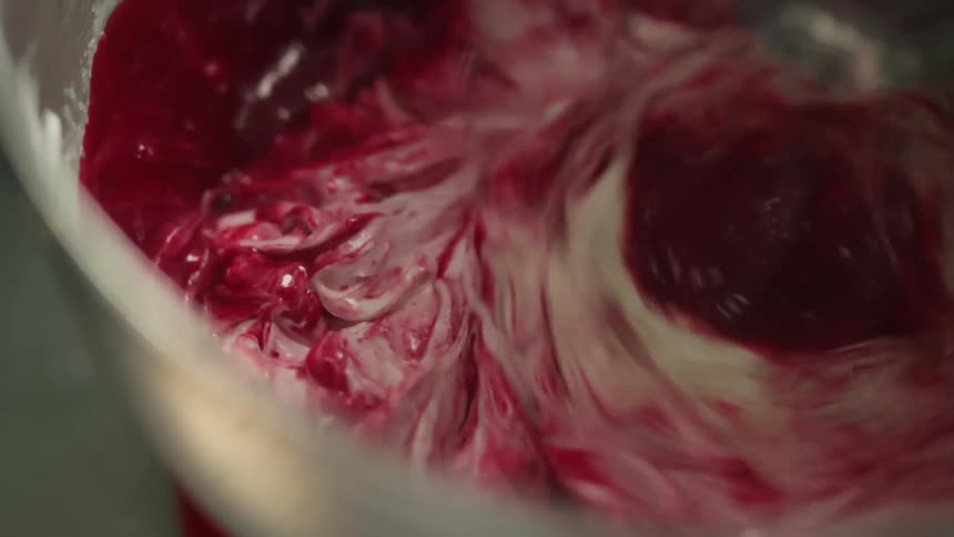 A dessert topping and a red substance being mixed in a bowl