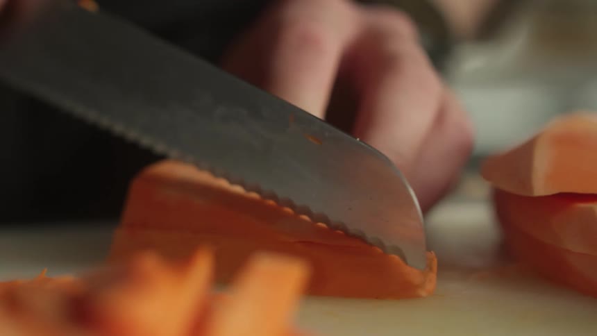 Close up of hands cutting and slicing a sweet potato on a cutting board