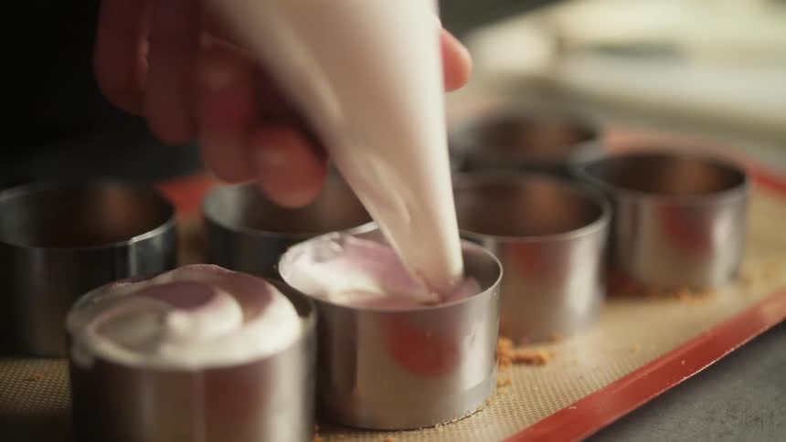 An employee at a restaurant fills small metal cups with icing
