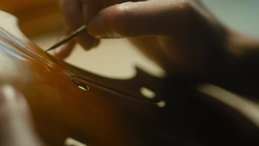 Female instrument maker paints part of a string instrument