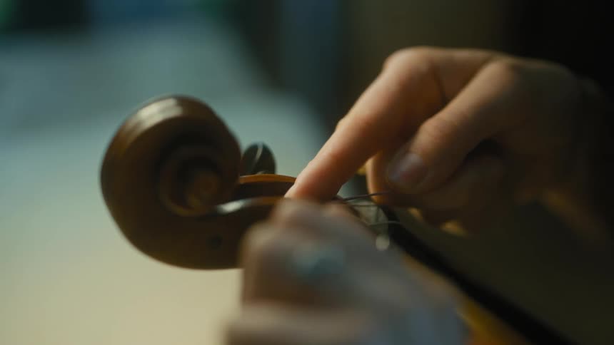 Closeup of hands turning the tuning pegs on a violin neck