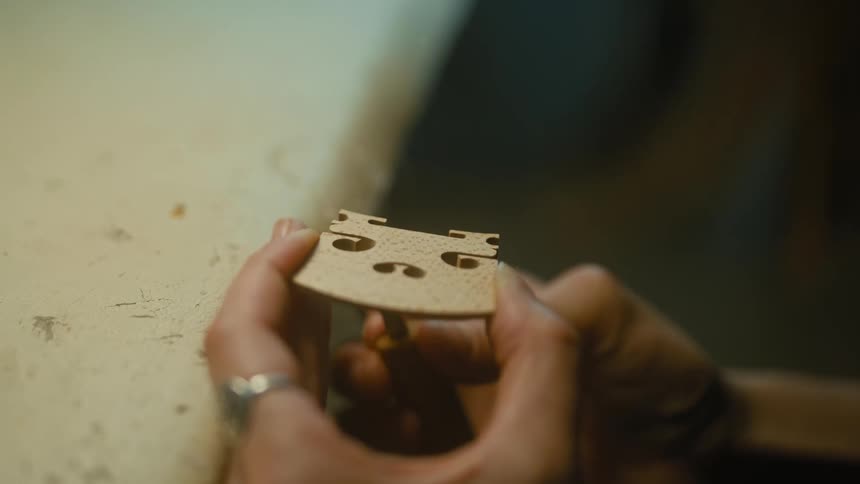 A luthier handcrafts and shapes the bridge of a violin