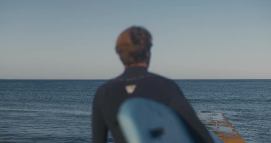 A man is holding his surfboard by the shore