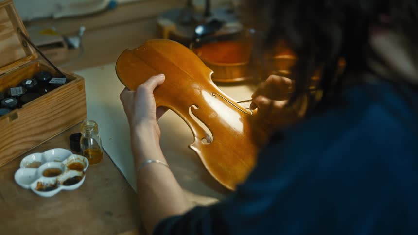 Closeup of a luthier painting the body of a violin