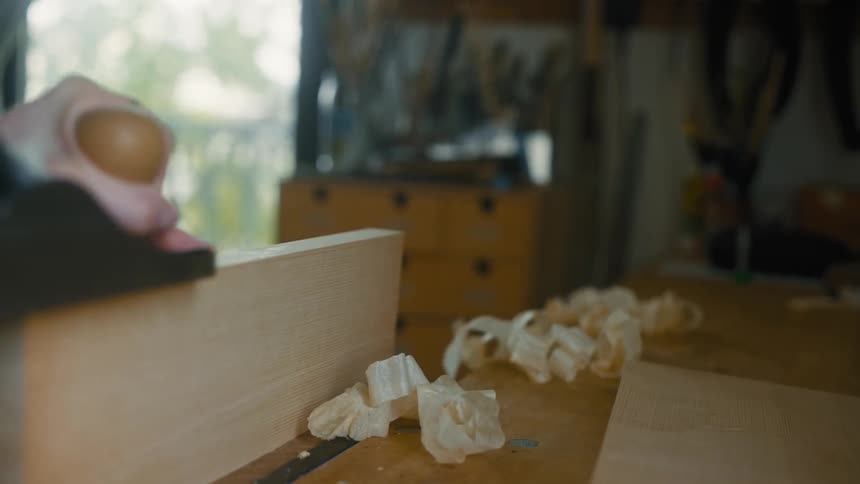 Hand using a chisel on a piece of wood with shavings scattered around