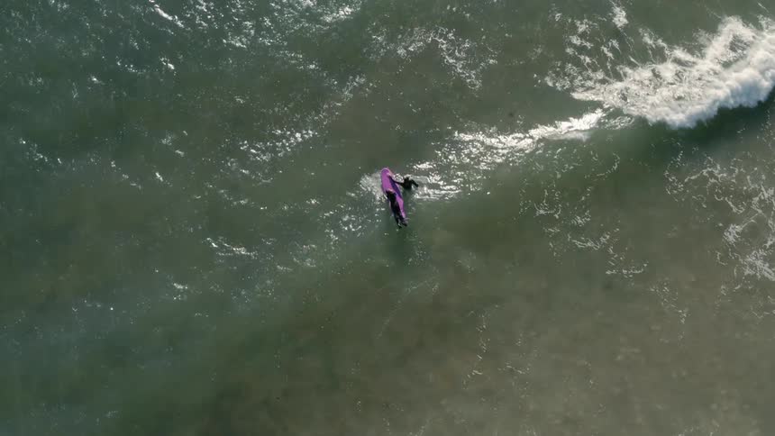 A surfer pushes a board out into the incoming tide