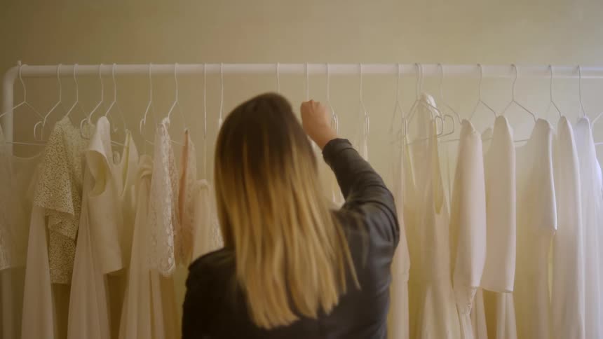 Blonde woman from behind choosing a white outfit on a hanger
