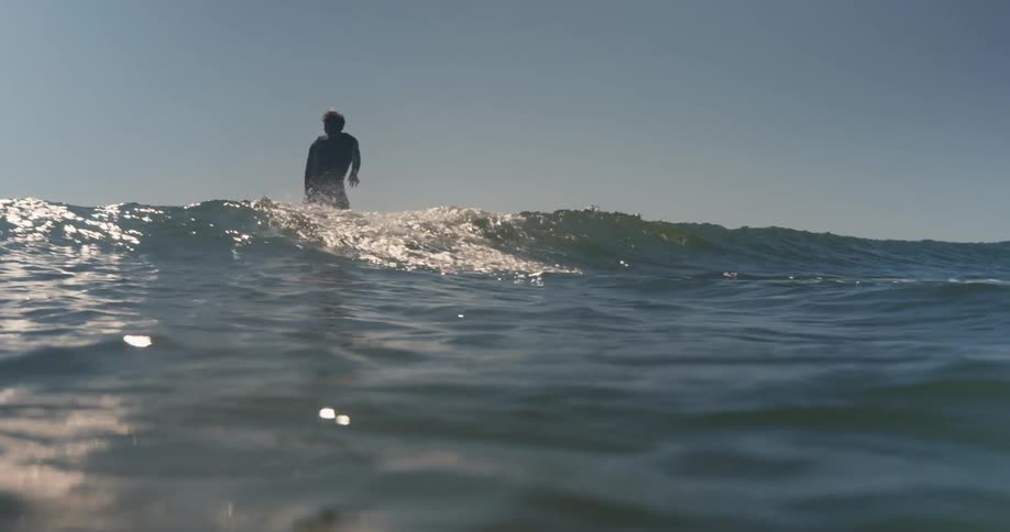 Surfer stands on his surfboard and rides a wave toward the beach on a sunny day