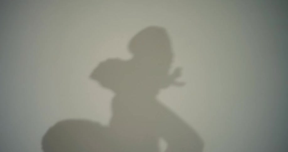 A female ballerina stretches her leg behind a white screen