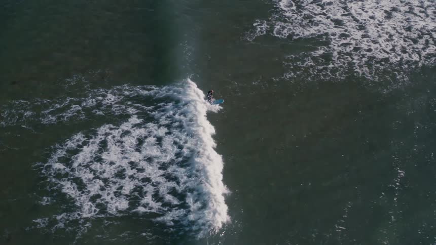 Aerial view of a person alone in the ocean surfing a wave