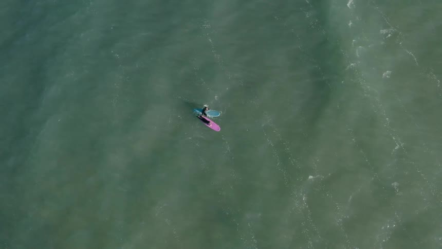 Aerial view of two people in the ocean with surfboards paddling