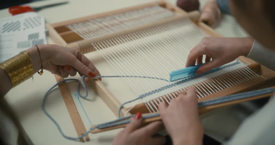 Hands working on a loom weaving with threads