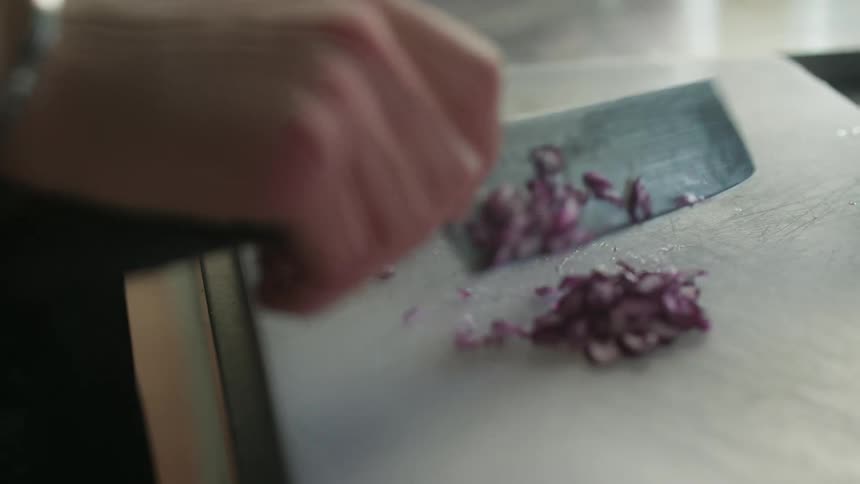A pair of hands chopping a red onion on a white cutting board with a large chefs knife