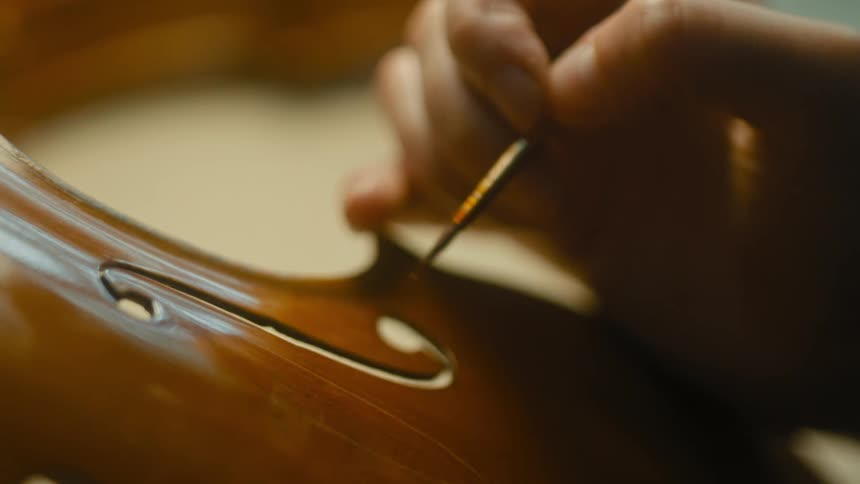 Hand holding a thin tool and shaping a violin