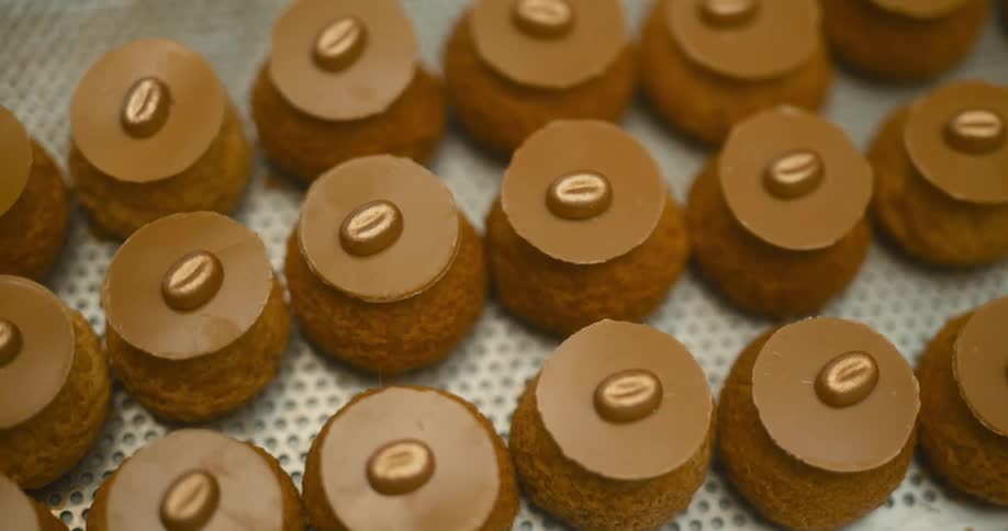 A tray of small round pastries covered in a brown glaze and topped with a single coffee bean