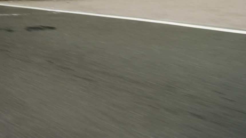 A close up of the cracked asphalt and white painted lines on a road seen from a moving vehicle