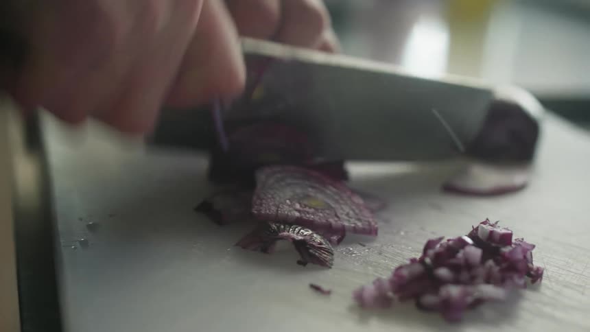 Hand with a knife cutting a red onion