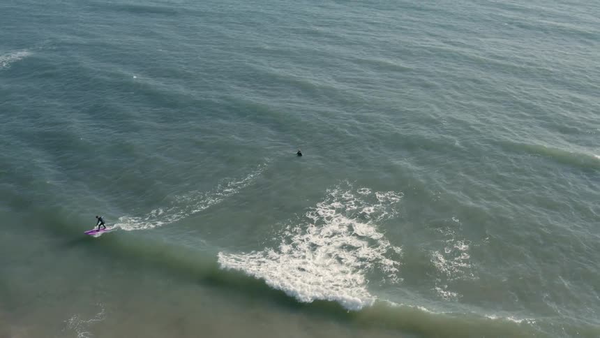 Overhead view of a person on a pink surfboard riding a wave