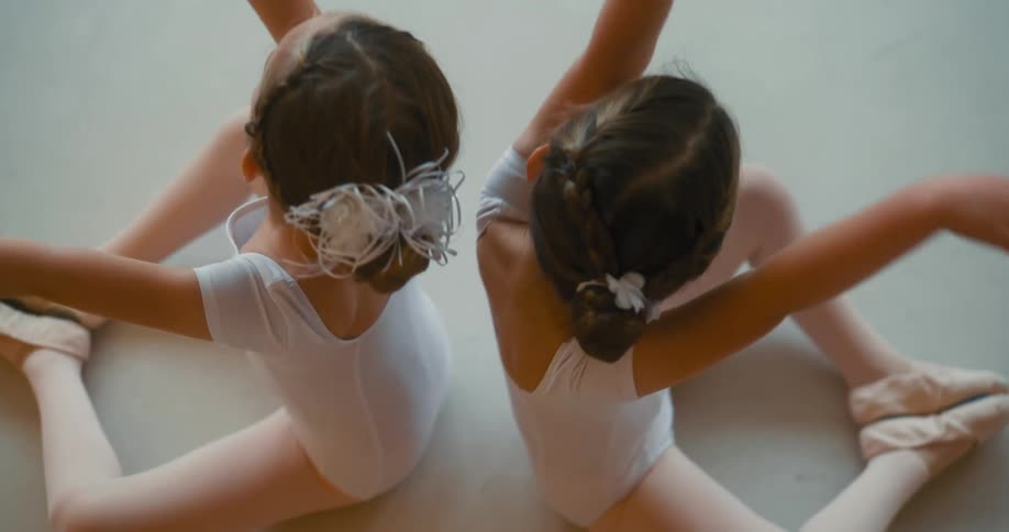 Two girls sitting back to back dancing ballet