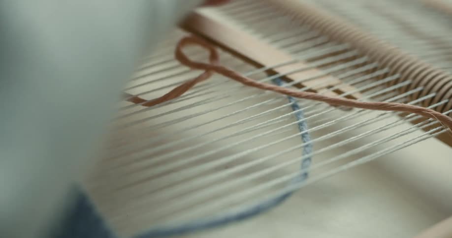 Hand passing yarn through a manual weaving machine