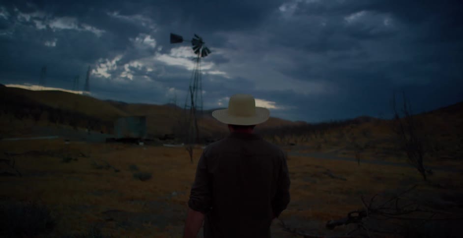 A solitary rancher in a cowboy hat walks on the ranch under a cloudy sky at dusk