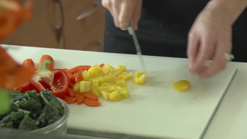 A woman cutting yellow peppers and adding them to a pile of red peppers and carrots
