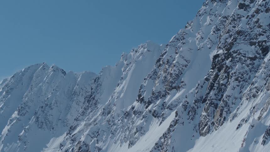 A snow covered mountain range stretches across a clear blue sky