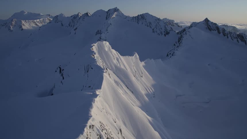 Sunlight illuminates a small portion of an extensive snowy mountain on a winter day