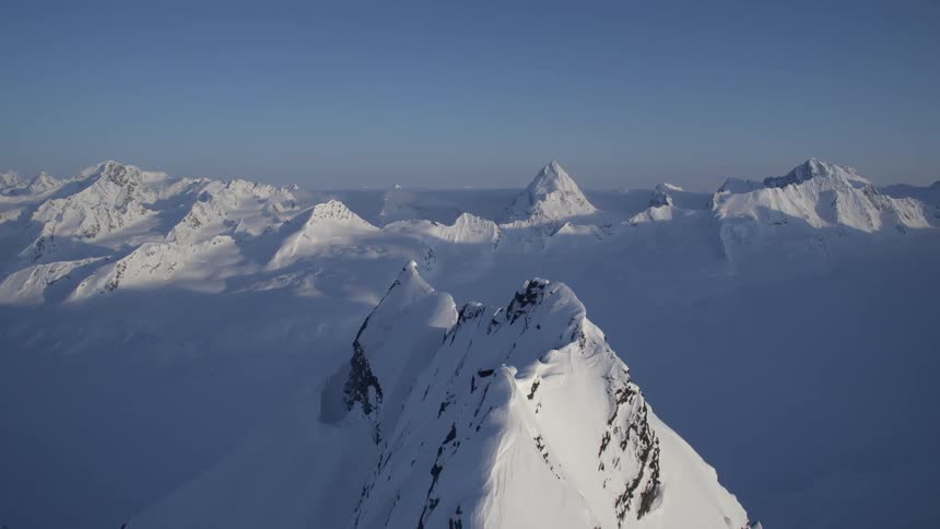 Aerial panorama of snowy mountain ranges against a clear blue sky