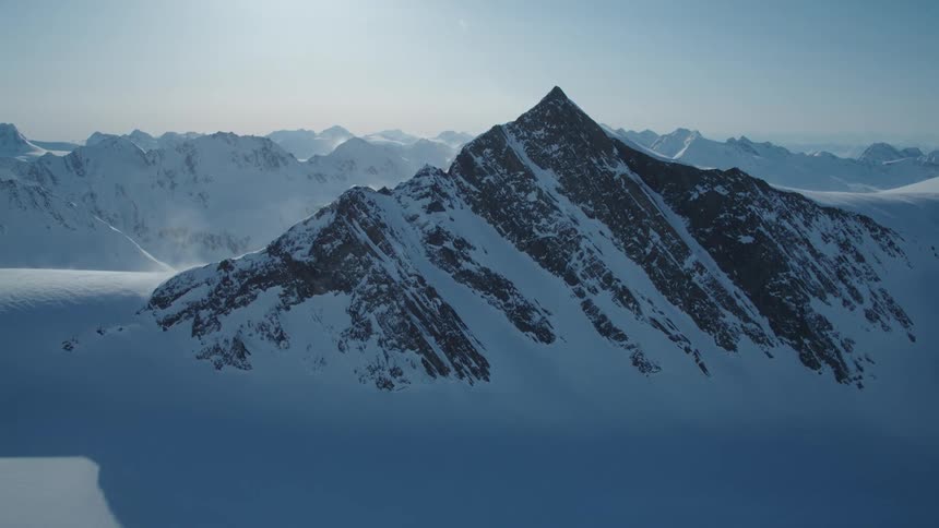 A solitary mountains covered in snow looms in front of large distant mountain ranges