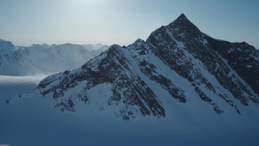 The sun shines down on a snow covered mountain and a range of mountains some distance away