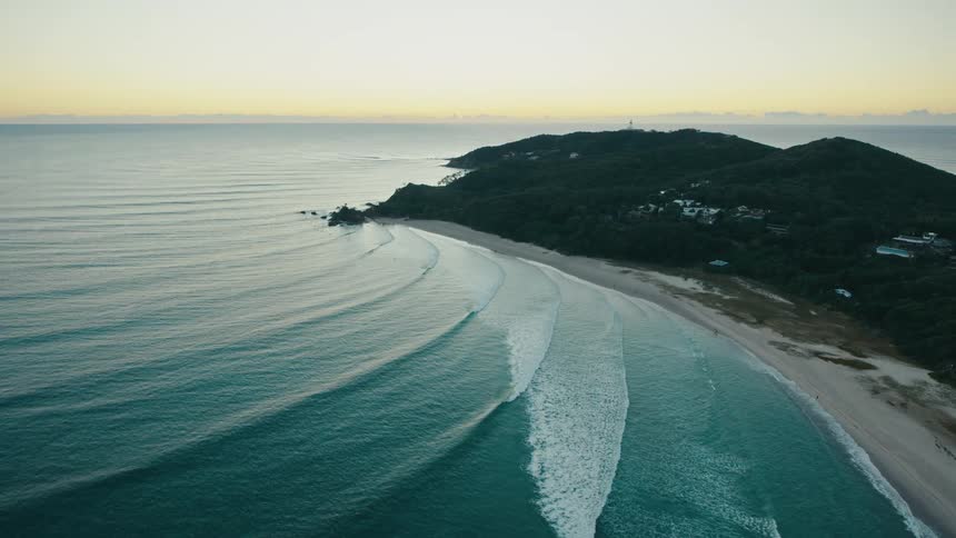 An aerial view of a secluded beach with rolling waves and a small island in the distance