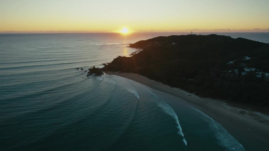 Aerial view of a sundrenched coastline where golden rays dance on the turquoise water highlighting rocky outcrops and a pristine sandy beach