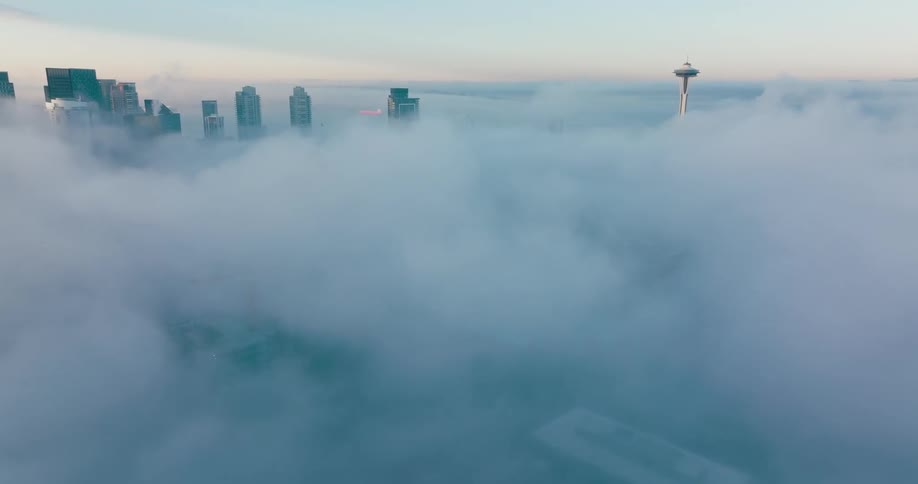 The tops of skyscrapers and the Space Needle peek through low clouds and fog shrouding the city below