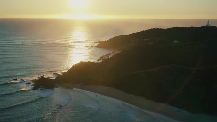 The sun casts a golden glow on the crystalclear water illuminating the rugged coastline and the pristine sandy beach