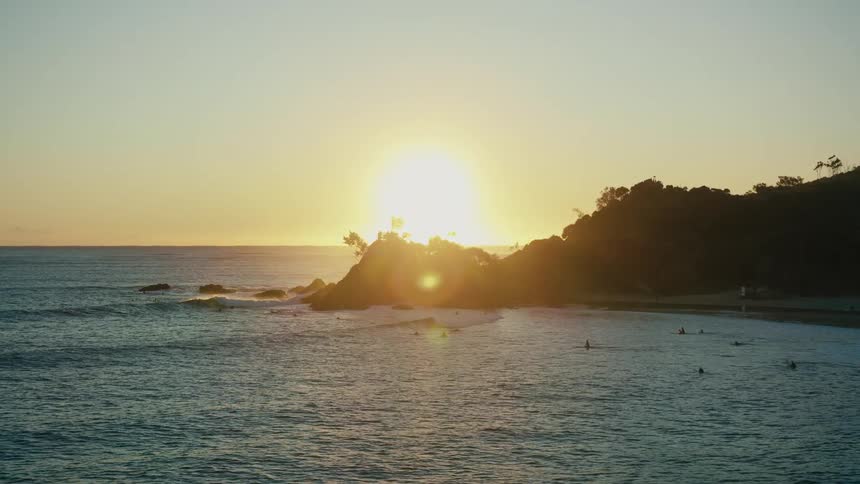 Aerial of a group of people surfing near an ocean shoreline at sunset
