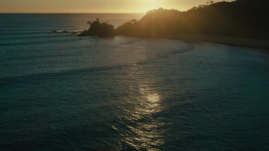 Aerial view of calm sea with rocky coastline in background and sunrise on horizon