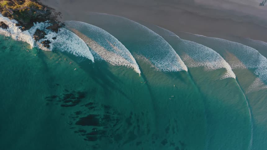 Aerial of a group of people surfing near the beach at sunset