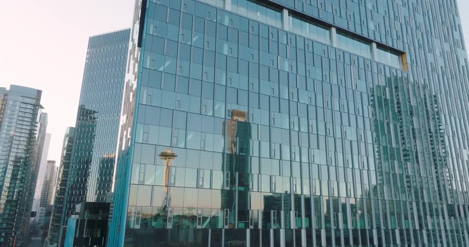 The Space Needle is reflected in the mirror like glass of a downtown office tower