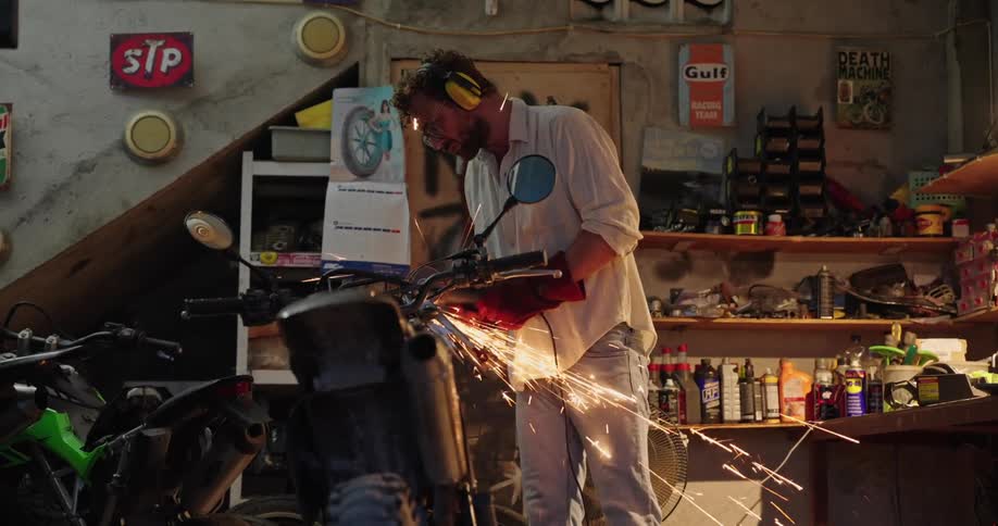A man uses a tool that emits sparks on a motorcycle in a shop